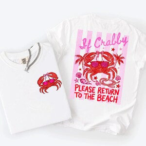K&ouml;nnte beinhalten: Zwei wei&szlig;e T-Shirts mit Krabbenmotiven. Ein Shirt hat eine kleine Krabbengrafik, das andere eine gr&ouml;&szlig;ere Krabbengrafik mit dem Text "If Crabby Please Return to the Beach". Die Krabbe tr&auml;gt eine Sonnenbrille.
