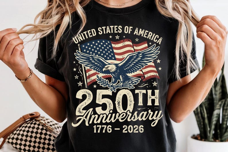 Pode incluir: Uma t-shirt preta de manga curta com um gr&aacute;fico de uma &aacute;guia-de-cabe&ccedil;a-branca em frente a uma bandeira dos Estados Unidos. O texto diz UNITED STATES OF AMERICA, 250TH Anniversary e 1776-2026. O design apresenta uma estampa desgastada vintage.