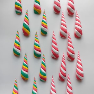 May include: A collection of cone-shaped objects are displayed against a white backdrop. Some are striped with red and white, others feature a spiral of green, yellow, pink, and white. The objects are arranged in a grid-like pattern, creating a visually appealing display.