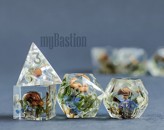 May include: Four clear resin dice with a nature theme. The dice are filled with dried flowers, leaves, and mushrooms. The dice are in the shape of a d4, d6, d8, and d20.