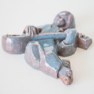 May include: A ceramic sculpture of a person playing a guitar. The sculpture is painted in shades of blue and brown.