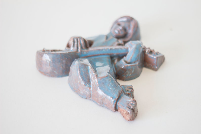 May include: A ceramic sculpture of a person playing a guitar. The sculpture is painted in shades of blue and brown.