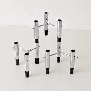 Peut inclure: Ensemble de six bougeoirs chromés au design minimaliste. Chaque bougeoir présente un corps cylindrique avec une base noire et une barre horizontale. Les bougeoirs sont disposés sur une surface blanche.
