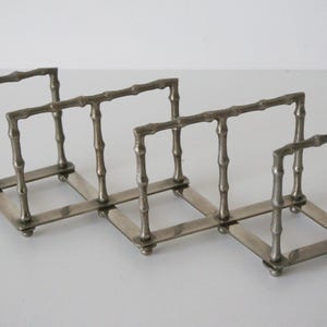 Könnte beinhalten: Ein silberfarbener, erweiterbarer Toastständer mit Bambus-Design. Der Ständer hat vier Abschnitte, jeweils mit quadratischer Basis und rechteckiger Oberseite, die durch scharnierartige Metallstreifen verbunden sind.