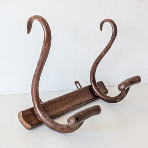 May include: A dark brown wooden wall-mounted coat rack featuring a horizontal rectangular base with two tall, curved upright hooks and two shorter, forward-extending hooks. The wood displays a worn, stained finish with visible grain texture.