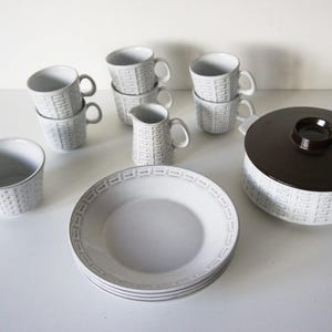 May include: A white ceramic dinnerware set with a textured basketweave pattern. The set includes mugs, a creamer, a bowl, plates, and a casserole dish with a brown lid. The dishes are arranged on a white surface.