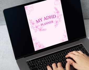 May include: A laptop computer displaying a pink digital planner with the text "MY ADHD PLANNER" on the screen. The laptop is on a gray surface and a person's hands are typing on the keyboard.