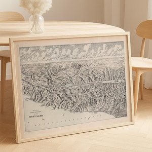 Puede incluir: Impresión enmarcada en blanco y negro del mapa de Tierra Santa, con detalles topográficos y el mar Mediterráneo. La impresión está en un marco de madera clara, apoyada contra una mesa de madera.
