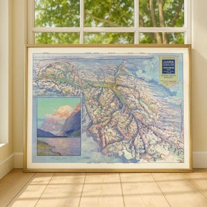 May include: A framed vintage map of Jasper National Park, featuring a detailed topographical view in shades of blue, green, and brown. The map includes a smaller inset image of a mountain landscape and lake. The frame is gold.
