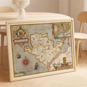 May include: Framed vintage map of Anglesey, with detailed illustrations of the island's geography, including towns, coastlines, and nautical elements. The map features a compass rose, ships, and decorative borders, presented in a wooden frame.