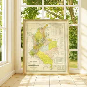 Puede incluir: Mapa antiguo enmarcado de Colombia, que muestra las regiones del país en amarillo, verde y rosa. El mapa está en un marco dorado y se apoya contra una ventana, con una vista de árboles.
