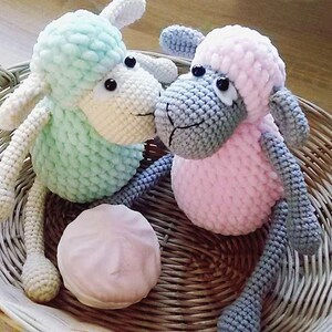 May include: Two crocheted stuffed sheep toys, one light green and one pink, sitting in a wicker basket.