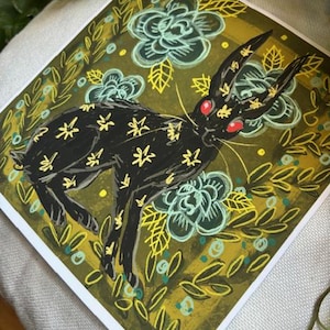 Pu&ograve; includere: Stampa artistica quadrata con un coniglio nero con segni gialli a forma di stella e occhi rossi. Il coniglio &egrave; ambientato su uno sfondo di fiori turchesi e fogliame verde oliva. L'opera d'arte ha uno stile illustrativo stravagante.