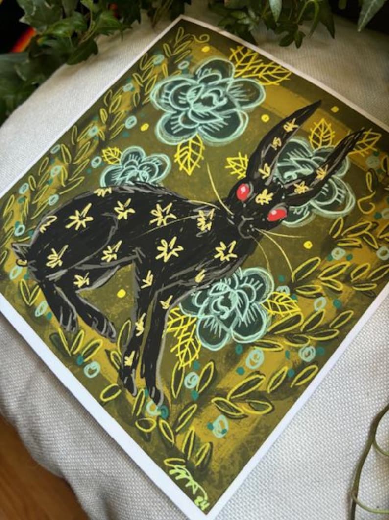 Pu&ograve; includere: Stampa artistica quadrata con un coniglio nero con segni gialli a forma di stella e occhi rossi. Il coniglio &egrave; ambientato su uno sfondo di fiori turchesi e fogliame verde oliva. L'opera d'arte ha uno stile illustrativo stravagante.