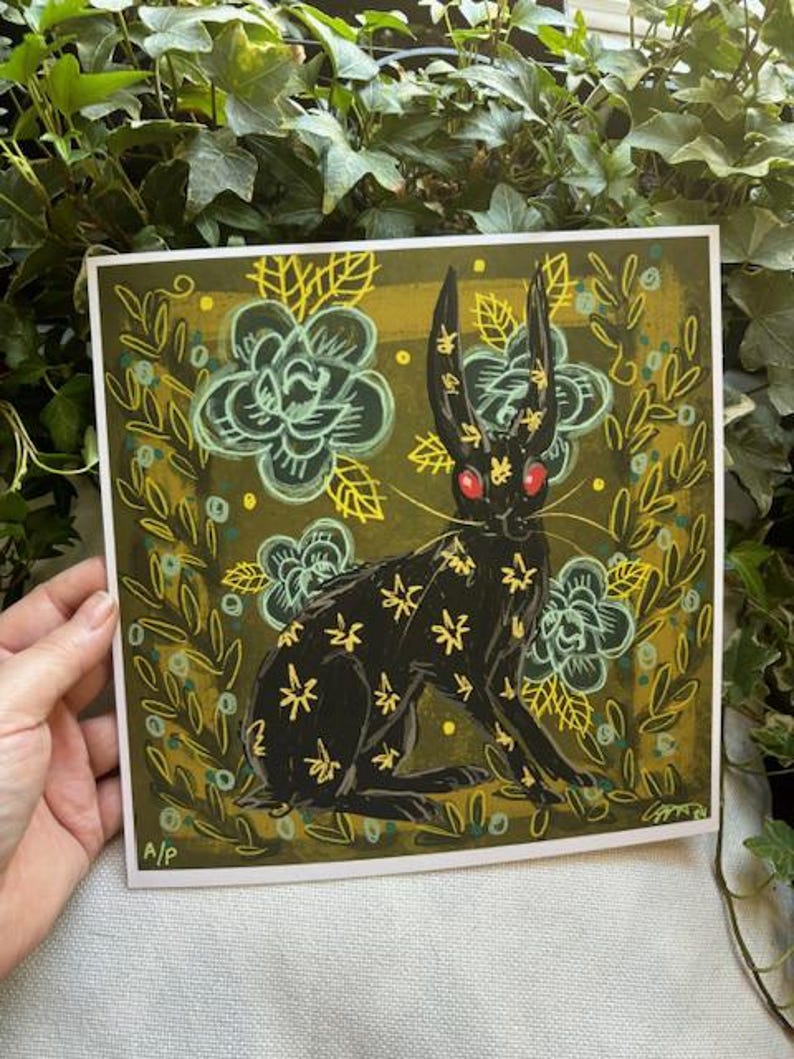 Pu&ograve; includere: Stampa artistica quadrata con un coniglio nero con accenti floreali gialli e occhi rossi. Il coniglio &egrave; ambientato su uno sfondo verde scuro con fiori e foglie stilizzati. La stampa ha uno stile illustrativo stravagante.