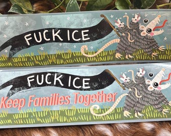 Könnte beinhalten: Zwei rechteckige Aufkleber mit hellblauem Hintergrund, mit dem Text "FUCK ICE" in Weiß auf einem schwarzen Banner. Ein Aufkleber hat auch den Text "Keep Families Together" in Rosa. Jeder Aufkleber hat eine Cartoon-Opossum-Illustration.
