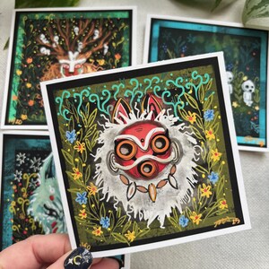 Puede incluir: Un conjunto de cuatro tarjetas ilustradas que presentan una m&aacute;scara roja y blanca con ojos naranjas, un &aacute;rbol con figuras blancas, una escena de bosque azul y verde y una figura blanca con un halo azul. Las tarjetas est&aacute;n impresas en papel blanco con bordes negros.
