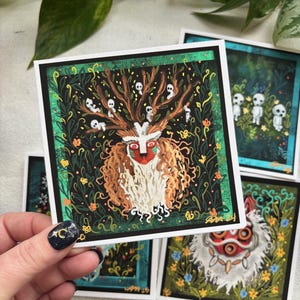 Puede incluir: Un conjunto de cuatro tarjetas ilustradas con personajes de la pel&iacute;cula animada 'La Princesa Mononoke'. Las tarjetas est&aacute;n impresas en cartulina blanca y tienen un borde negro. La primera tarjeta presenta una criatura blanca y peluda con una m&aacute;scara roja y negra, rodeada de follaje verde y peque&ntilde;as figuras blancas fantasmales. La segunda tarjeta presenta una criatura blanca y peluda con una m&aacute;scara roja, rodeada de follaje verde y flores azules. La tercera tarjeta presenta un grupo de peque&ntilde;as figuras blancas fantasmales de pie en un bosque. La cuarta tarjeta presenta una criatura blanca y peluda con una m&aacute;scara roja, rodeada de follaje verde y flores azules.
