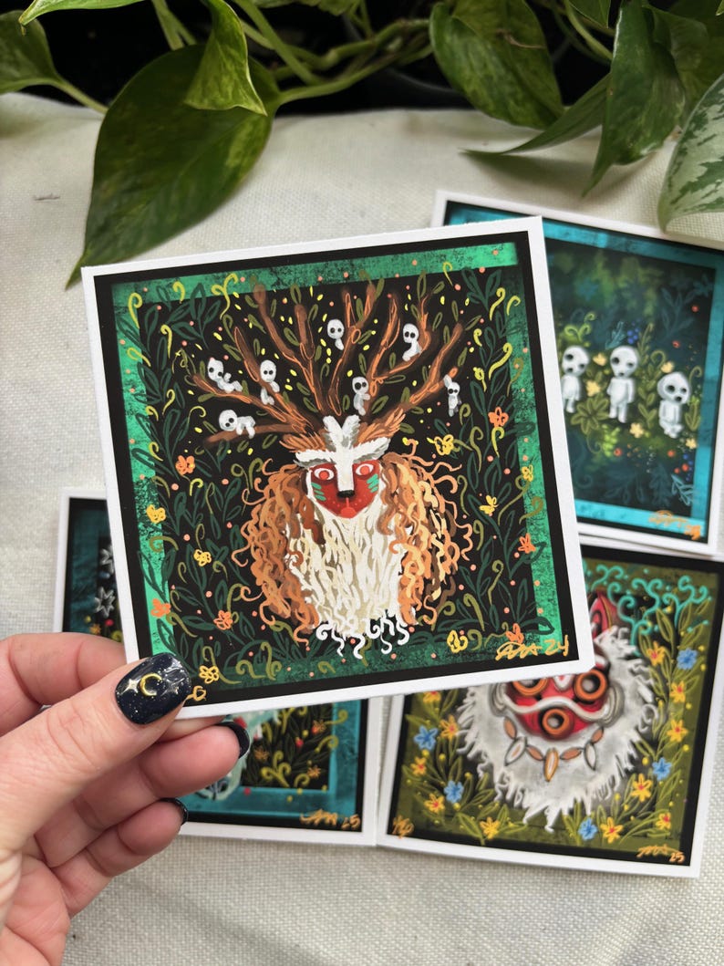 Puede incluir: Un conjunto de cuatro tarjetas ilustradas con personajes de la pel&iacute;cula animada 'La Princesa Mononoke'. Las tarjetas est&aacute;n impresas en cartulina blanca y tienen un borde negro. La primera tarjeta presenta una criatura blanca y peluda con una m&aacute;scara roja y negra, rodeada de follaje verde y peque&ntilde;as figuras blancas fantasmales. La segunda tarjeta presenta una criatura blanca y peluda con una m&aacute;scara roja, rodeada de follaje verde y flores azules. La tercera tarjeta presenta un grupo de peque&ntilde;as figuras blancas fantasmales de pie en un bosque. La cuarta tarjeta presenta una criatura blanca y peluda con una m&aacute;scara roja, rodeada de follaje verde y flores azules.
