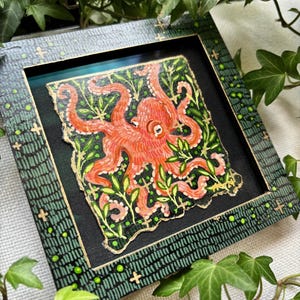 May include: A framed painting of an orange octopus with green leaves on a black background. The frame is green with gold accents.