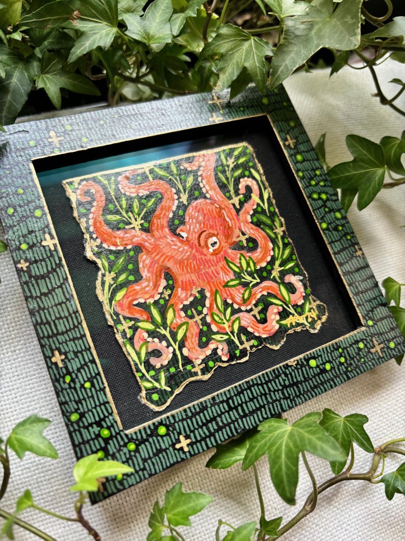 May include: A framed painting of an orange octopus with green leaves on a black background. The frame is green with gold accents.