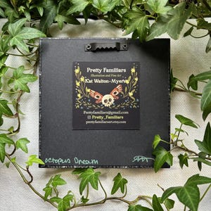 May include: A black framed print with a colorful illustration of a skull with butterfly wings. The print has the title "octopus Dream" and the artist's information: "Pretty Familiars, Illustration and Fine Art, Kat Walton-Myer's, Prettyfamiliars@gmail.com, Pretty_Familiars, prettyfamiliarsart.etsy.com".