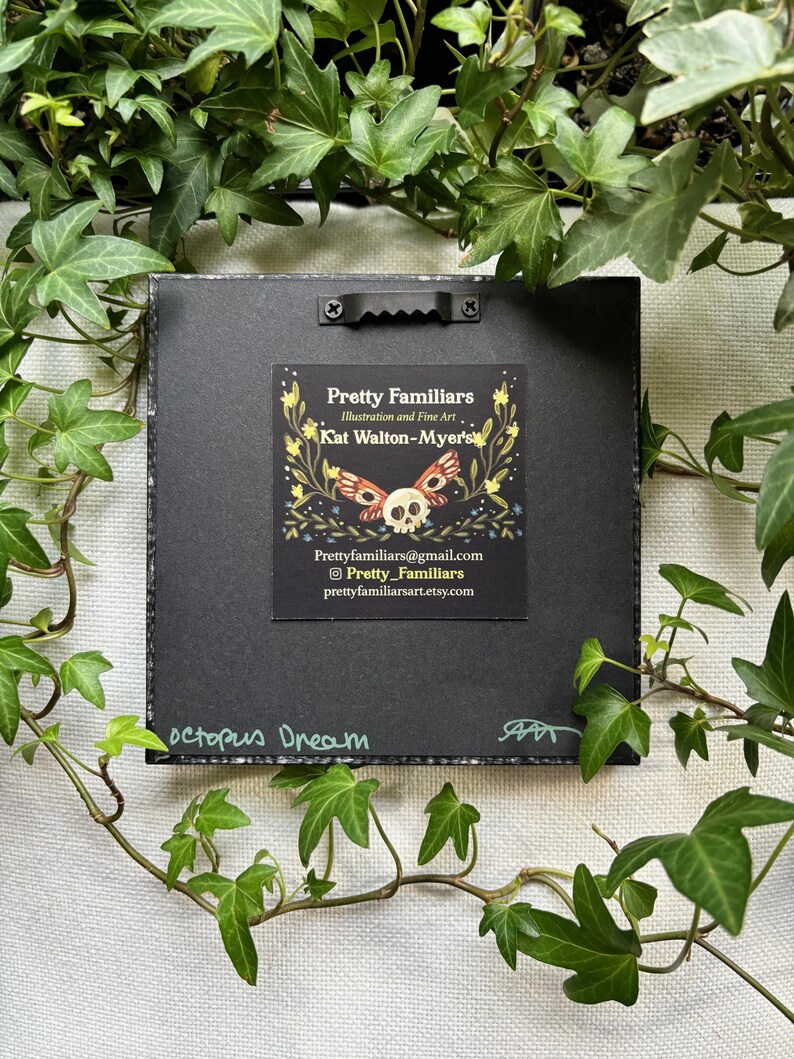 May include: A black framed print with a colorful illustration of a skull with butterfly wings. The print has the title "octopus Dream" and the artist's information: "Pretty Familiars, Illustration and Fine Art, Kat Walton-Myer's, Prettyfamiliars@gmail.com, Pretty_Familiars, prettyfamiliarsart.etsy.com".