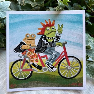 May include: Two frogs riding a red tandem bicycle. The frog in the front has green skin, a mohawk, and is wearing a black leather jacket. The frog in the back has brown skin and is wearing a black leather jacket and a red and black plaid kilt.