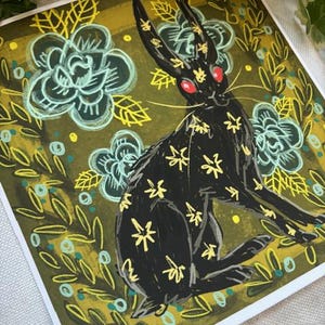 Pu&ograve; includere: Stampa artistica quadrata con un coniglio nero con motivi floreali gialli e occhi rossi. Il coniglio &egrave; ambientato su uno sfondo di fiori turchesi e fogliame verde oliva. L'opera d'arte ha uno stile illustrativo stravagante.