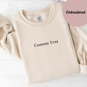 May include: A beige sweatshirt with the text "Custom Text" embroidered on the front.