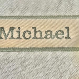 May include: A white fabric label with a green border and the name "Michael" embroidered in green.
