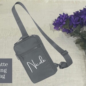 May include: A grey matte sling bag with an adjustable strap. The bag has a white inscription that says "Nicole".