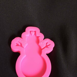 K&ouml;nnte beinhalten: Rosa Silikonform in Form eines Schneemanns mit den Worten "Angel Wings" an den Armen.