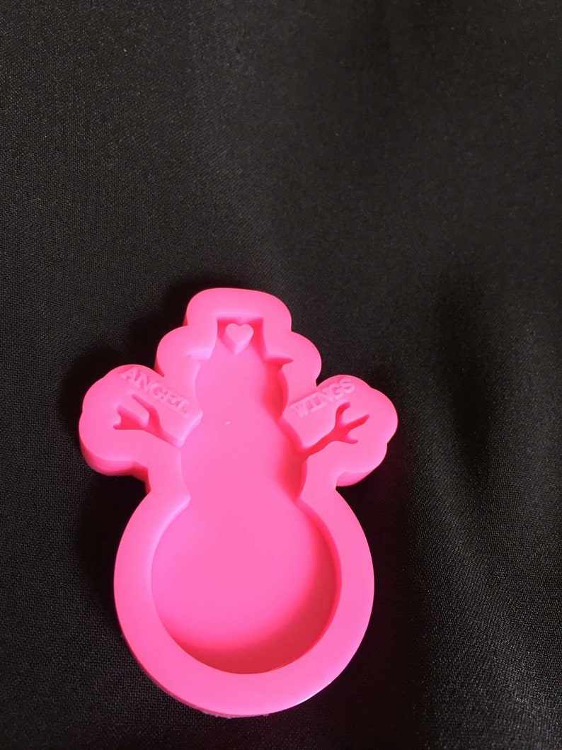 K&ouml;nnte beinhalten: Rosa Silikonform in Form eines Schneemanns mit den Worten "Angel Wings" an den Armen.