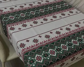 Puede incluir: Mantel blanco con un patrón geométrico verde y rosa. El mantel está puesto sobre una mesa con dos sillas.