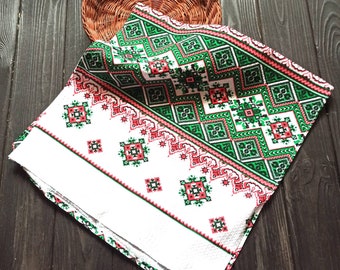 Puede incluir: Toalla de cocina blanca bordada con un patrón geométrico verde y rojo. La toalla tiene un borde decorativo.