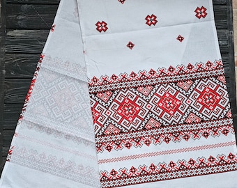 Puede incluir: Mantel de mesa de lino blanco con patrones geométricos bordados en rojo y negro. El mantel tiene un diseño tradicional con una banda central de patrones intrincados y patrones repetitivos más pequeños en la parte superior e inferior.