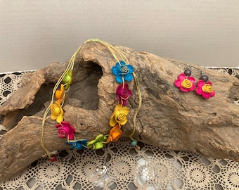 May include: A colorful flower necklace and matching earrings made of paper. The necklace is made of a string of colorful paper flowers, and the earrings are made of two pink paper flowers.