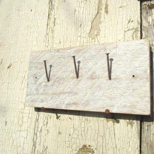 Könnte beinhalten: Ein verwittertes Holzschild mit der römischen Ziffer 'IV' in schwarzer Farbe. Das Schild ist mit rostigen Nägeln an einer weiß gestrichenen Holzoberfläche befestigt.