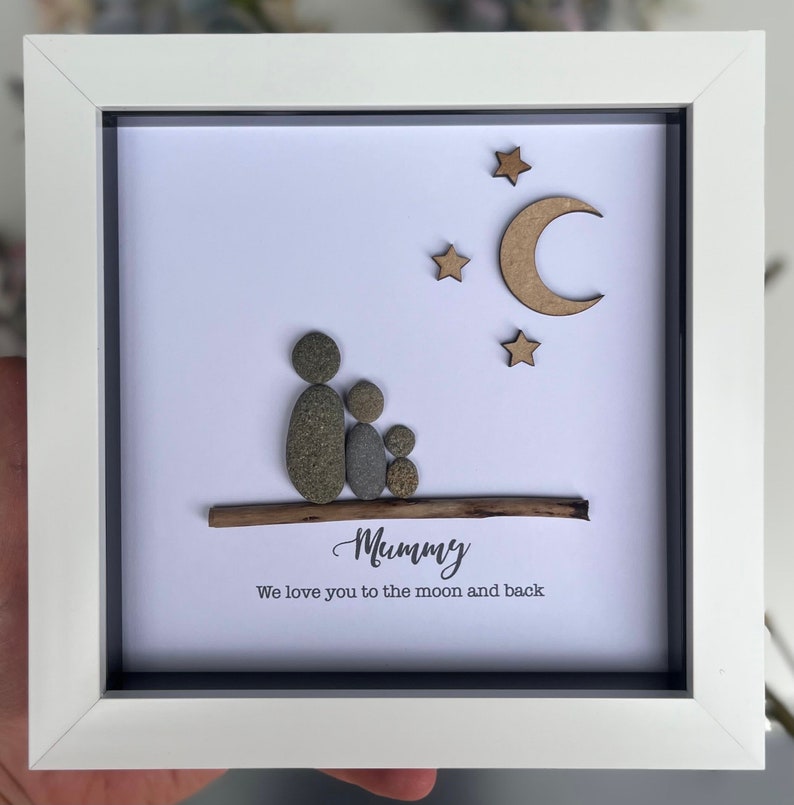 May include: A framed pebble art piece with a family of four, a moon and stars, and the text "Mummy We love you to the moon and back".