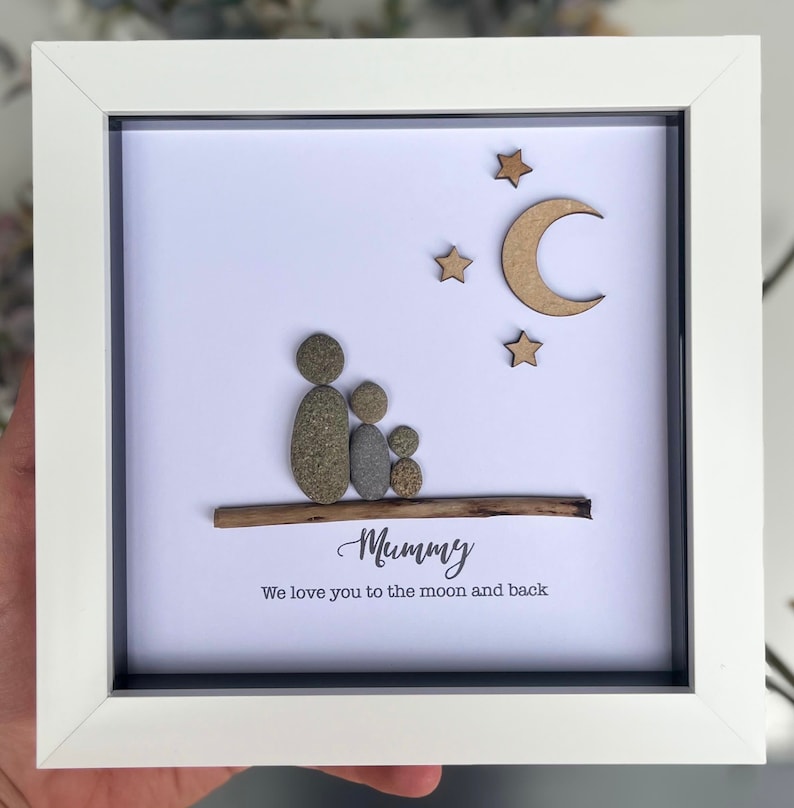 May include: A framed pebble art picture with a family of three, a moon and stars, and the text "Mummy We love you to the moon and back".