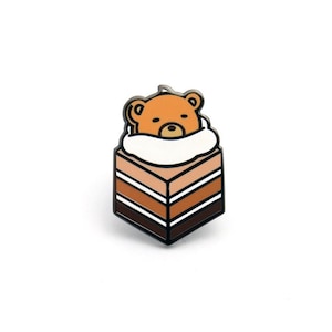 May include: A brown bear wearing a white hat is inside a layered cake with brown, orange, and white frosting. The cake is in a square shape and has a black outline.