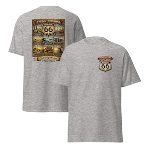 Puede incluir: Dos camisetas grises. Una presenta un gran gráfico de la Ruta 66 en la parte posterior con el texto "The Mother Road" y "Route 66". El gráfico incluye imágenes de puntos de referencia y el texto "Celebrating 100 years! 1926-2026". La otra camiseta tiene un logotipo de la Ruta 66 más pequeño en la parte delantera.
