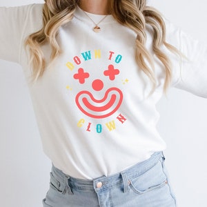May include: White sweatshirt with a colorful graphic of a clown face and the text "Down to Clown".