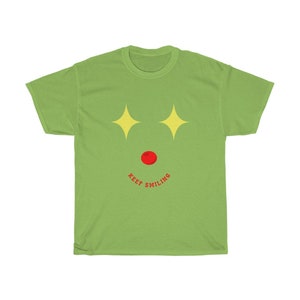 Puede incluir: Camiseta verde con un dise&ntilde;o de cara de dibujos animados. La cara tiene estrellas amarillas para los ojos, una nariz roja y una sonrisa roja con el texto "KEEP SMILING" debajo.