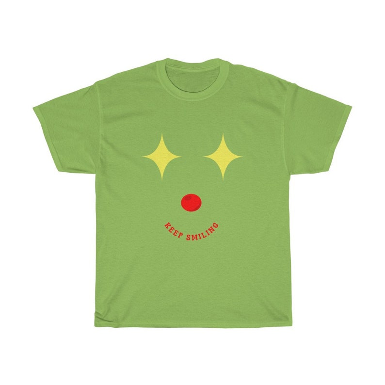 Puede incluir: Camiseta verde con un dise&ntilde;o de cara de dibujos animados. La cara tiene estrellas amarillas para los ojos, una nariz roja y una sonrisa roja con el texto "KEEP SMILING" debajo.