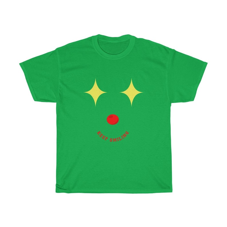 Puede incluir: Camiseta verde con un gr&aacute;fico de cara sonriente. La cara tiene estrellas amarillas para los ojos, una nariz roja y el texto "KEEP SMILING" debajo.