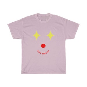 Puede incluir: Una camiseta de color morado claro con un dise&ntilde;o de estrellas amarillas y el texto "KEEP SMILING" en rojo.