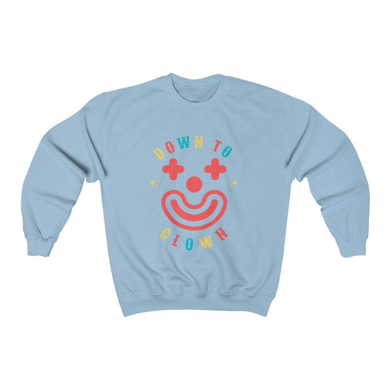 May include: A light blue sweatshirt with the text "DOWN TO CLOWN" in a rainbow color scheme. A red clown face with a smile and two plus signs for eyes is in the center of the text.