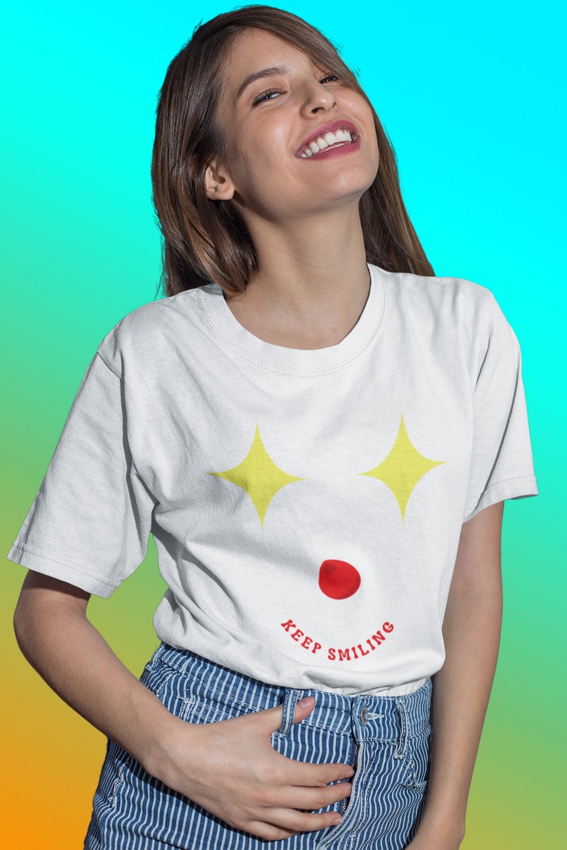 Puede incluir: Una camiseta blanca con un gr&aacute;fico de cara sonriente amarilla y el texto "KEEP SMILING". La modelo lleva pantalones a rayas azules y blancas y sonr&iacute;e.